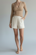 Woman wearing a beige long-sleeve top and white shorts against a plain background