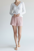 Woman wearing a white long-sleeve top and pink shorts against a plain background